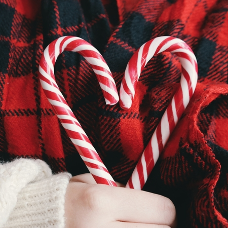 Two candy canes held across each other in a heart shape by a person wearing a plaid jacket.