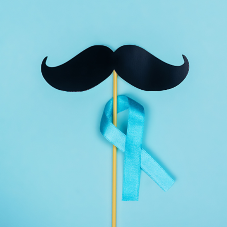 A paper cutout of a curly black moustache attached to a stick with a blue men's health ribbon wrapped around it.